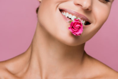 nach behandlung mit botox lächelt junge frau mit rose im mund isoliert vor rosa hintergrund